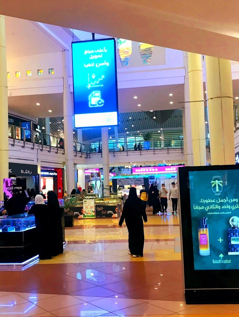 People walking in a brightly lit shopping mall with digital screens displaying advertisements.