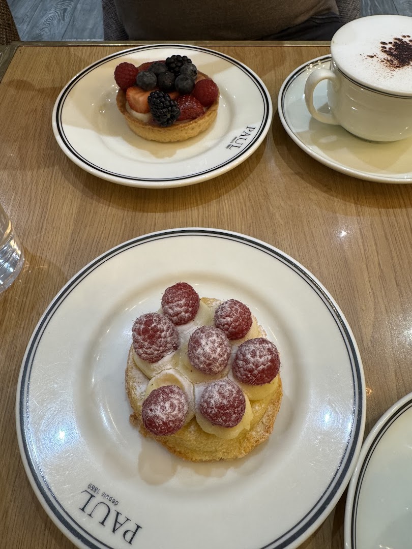 Two delicious fruit tarts and a cappuccino are displayed on a wooden table.
