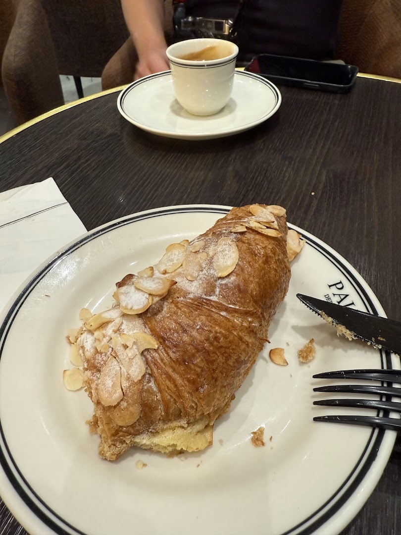 A close-up of an almond croissant and a cup of espresso on a table.