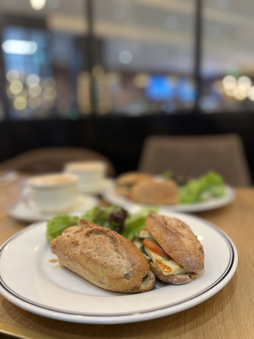 A close-up of two sandwiches with salad and coffee cups in the background.