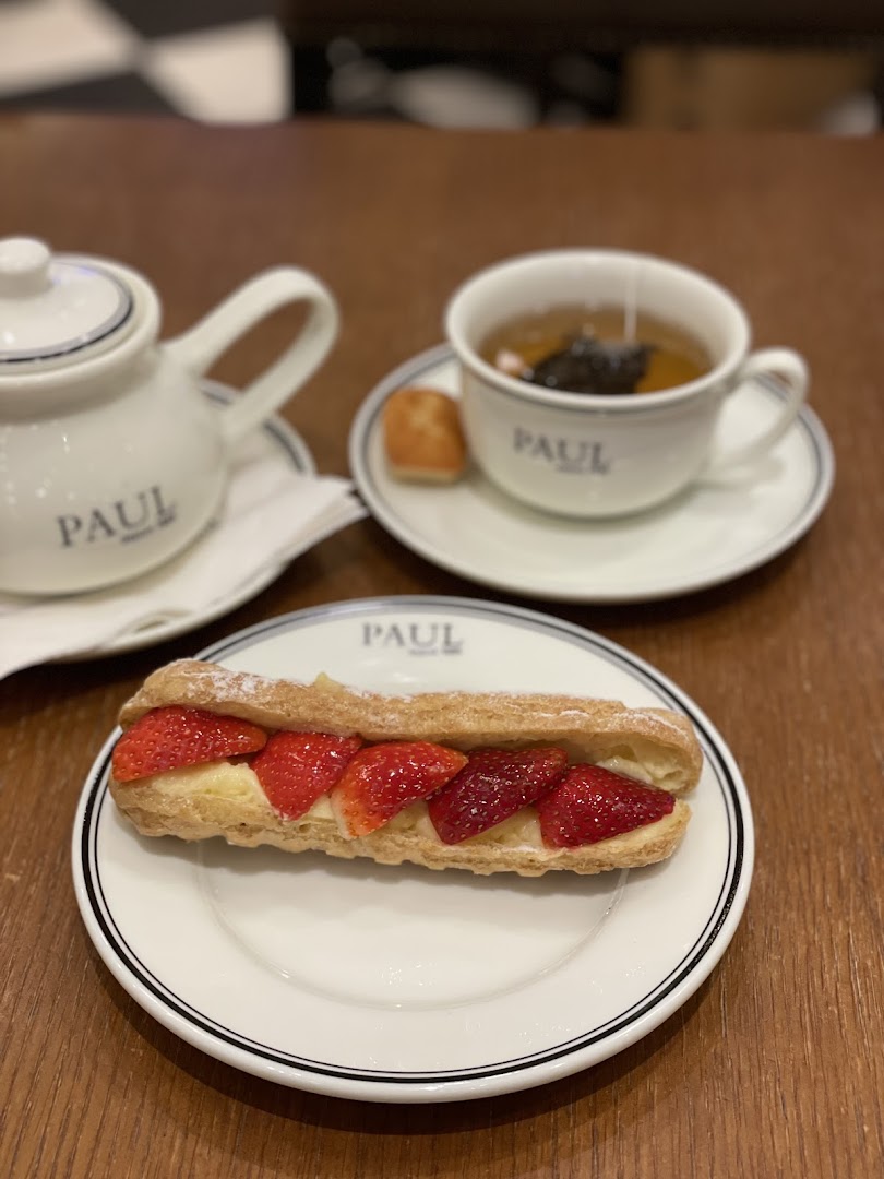 A strawberry eclair and a cup of tea are served on a wooden table.