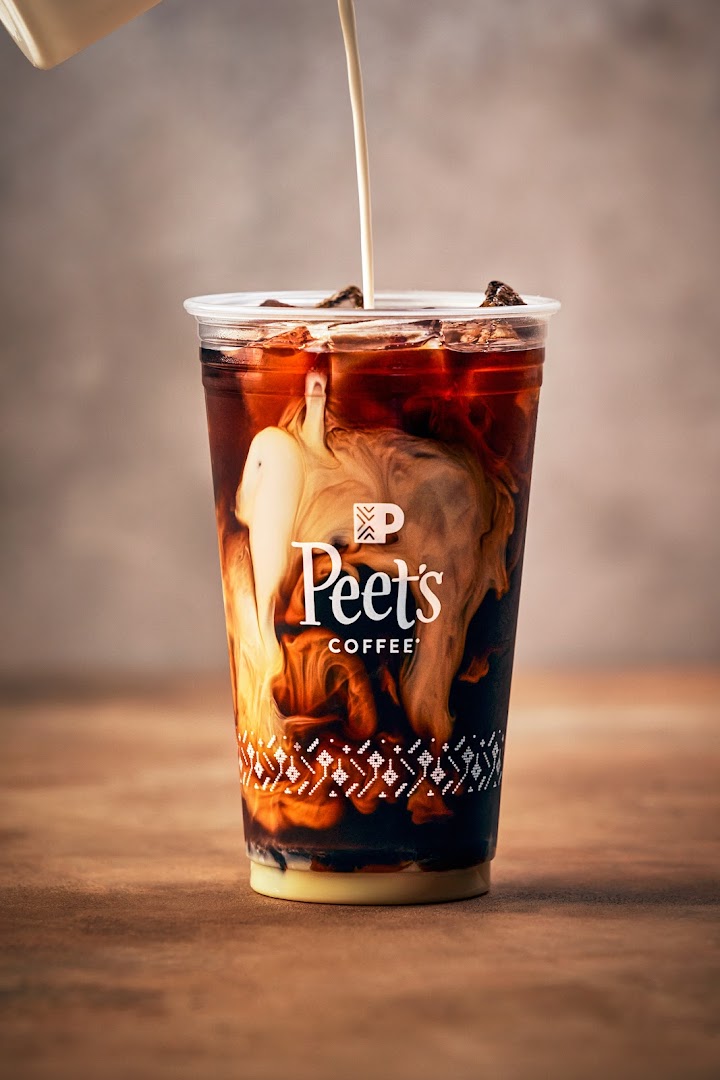 A close-up of a Peet's Coffee iced beverage with cream being poured in.