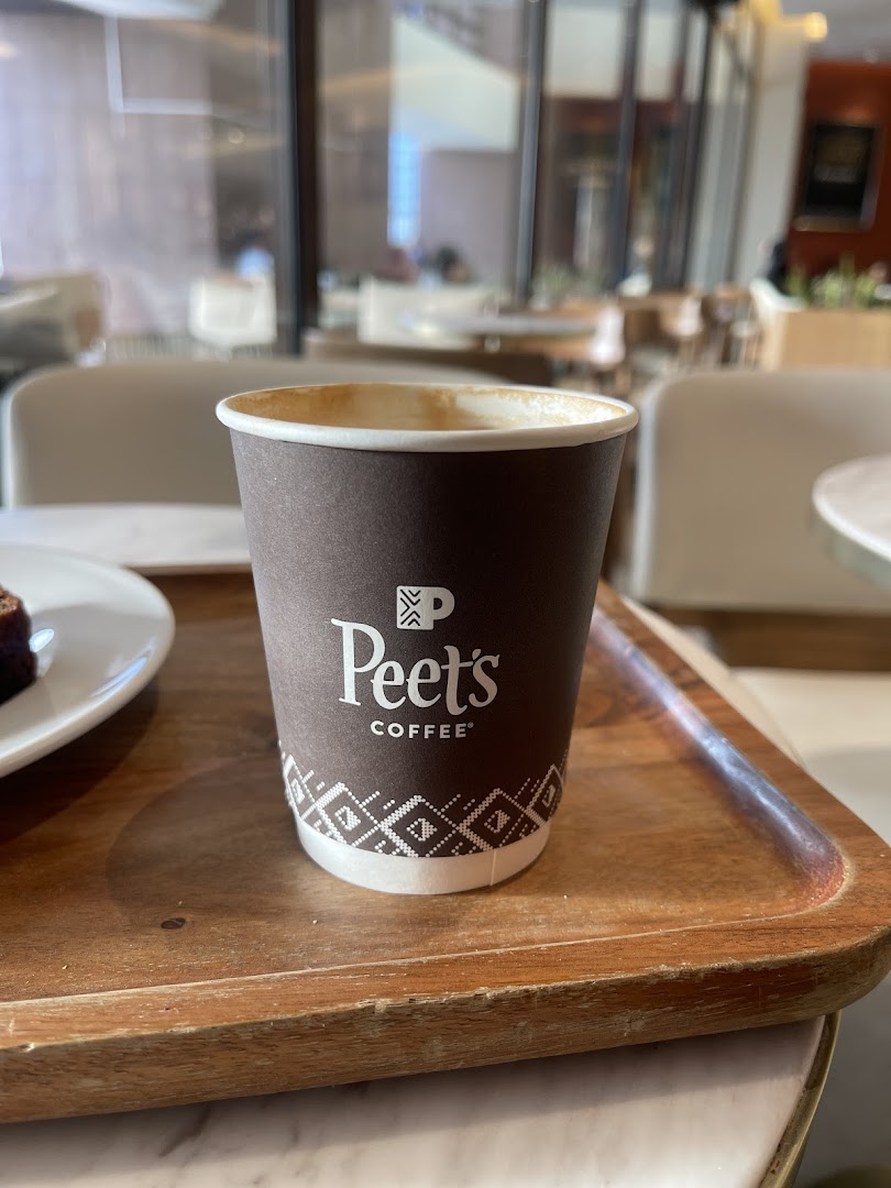 A close-up of a Peet's Coffee cup on a wooden tray with a pastry in the background.