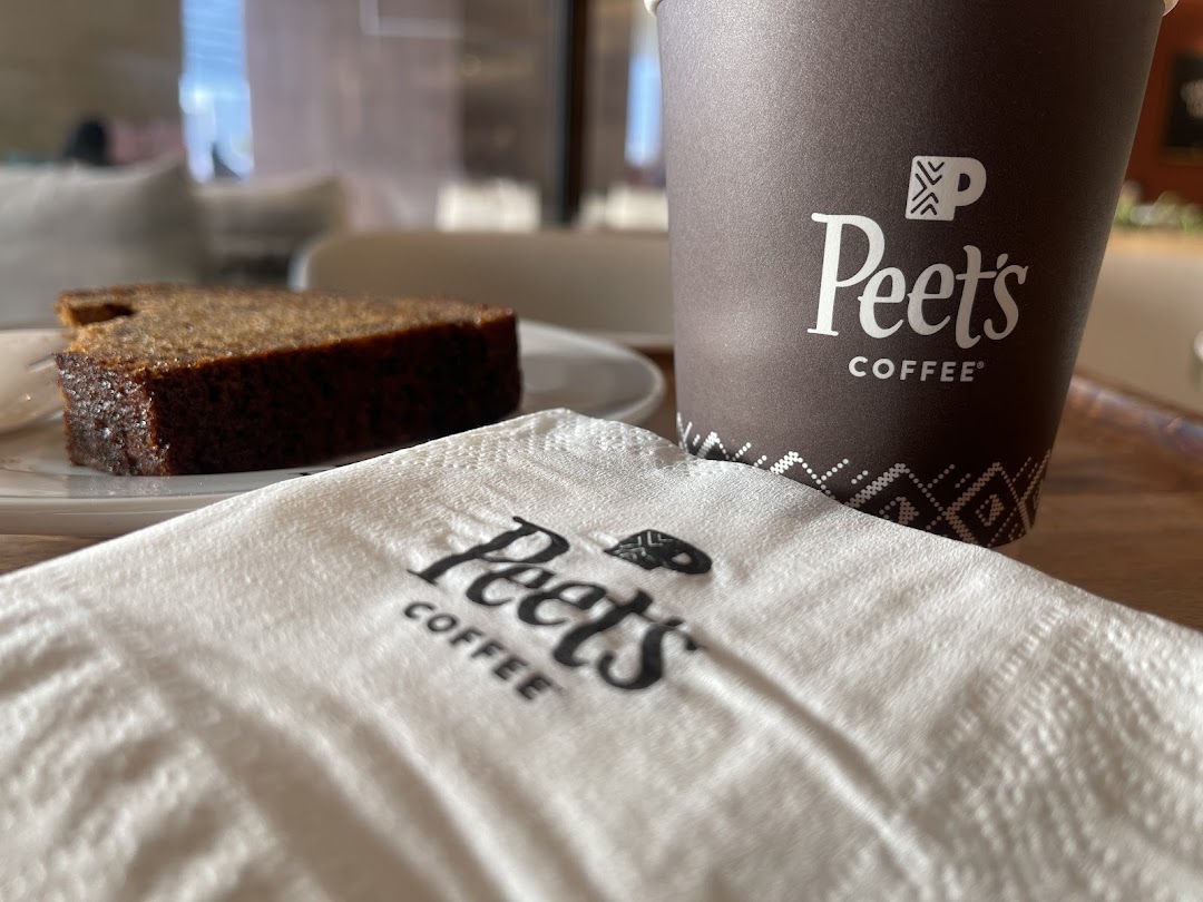 A slice of cake and a Peet's Coffee cup on a table.
