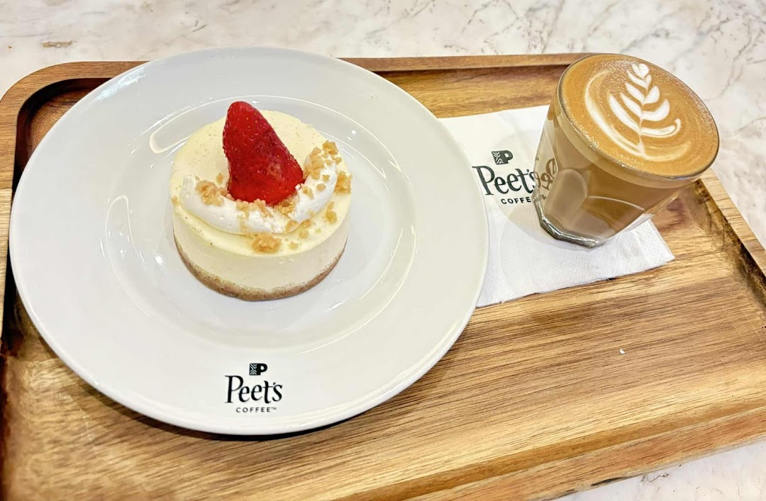 A delicious cheesecake with strawberry and whipped cream, served with a latte on a wooden tray.