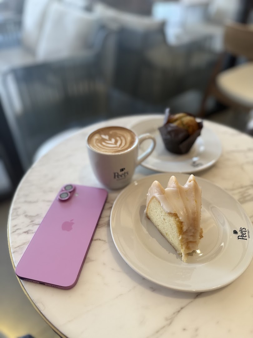 A slice of cake and a latte are on a marble table next to a pink phone.