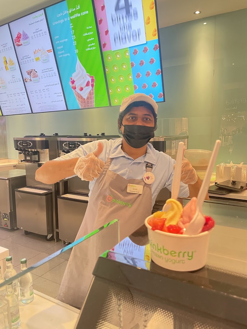 A Pinkberry employee gives a thumbs up next to a cup of frozen yogurt with fruit.