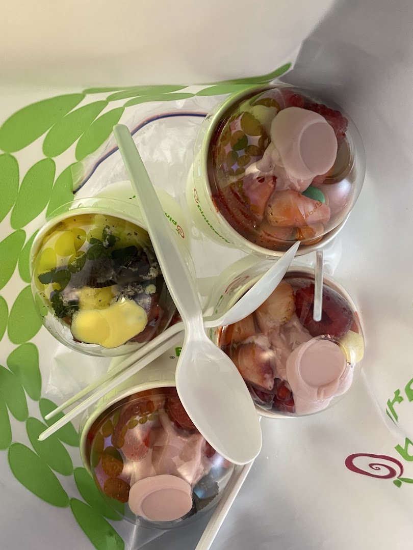 Three cups of Pinkberry frozen yogurt with fruit toppings and spoons.