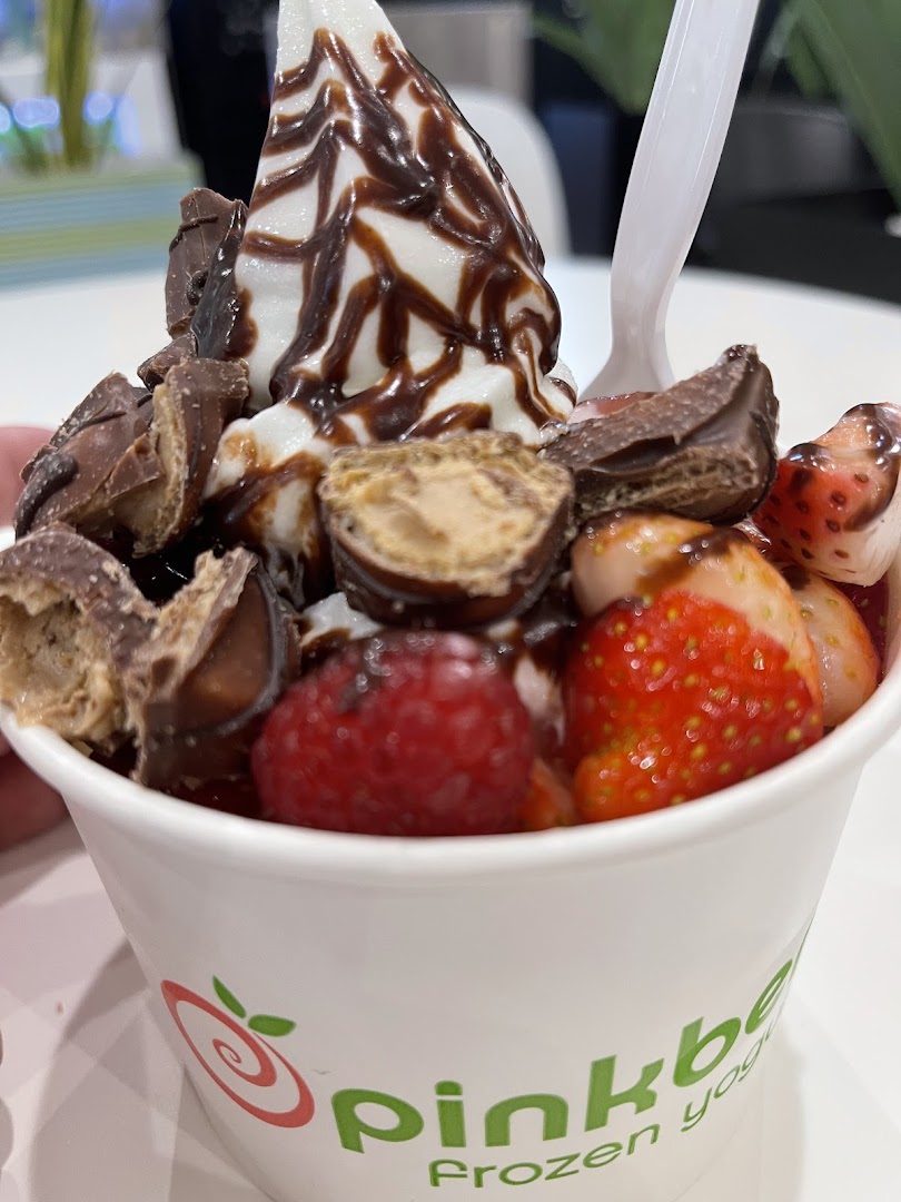 A cup of frozen yogurt topped with chocolate sauce, strawberries, raspberries, and candy pieces.