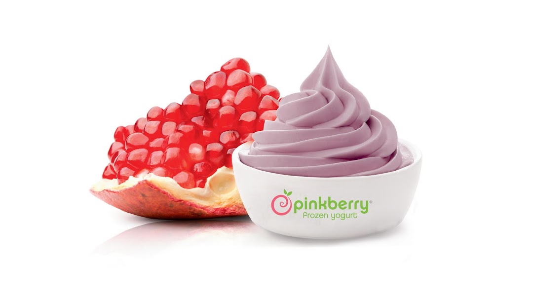 A bowl of pink frozen yogurt next to a slice of pomegranate.