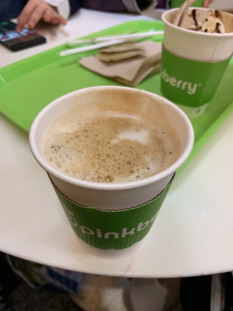 A close-up of a frothy coffee drink with a Pinkberry branded cup sleeve.