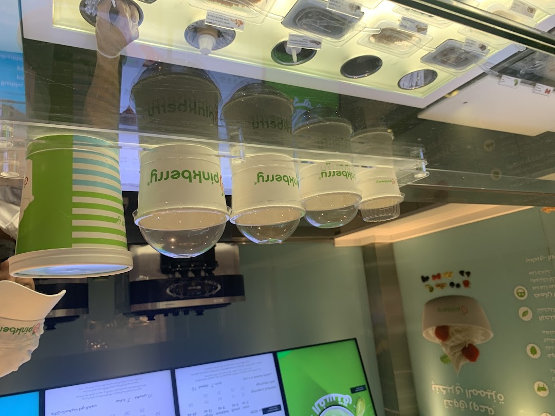 A display of Pinkberry frozen yogurt cups and toppings behind a glass counter.