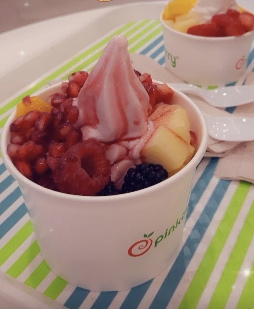 Two cups of frozen yogurt topped with fresh fruits and a swirl of sauce.