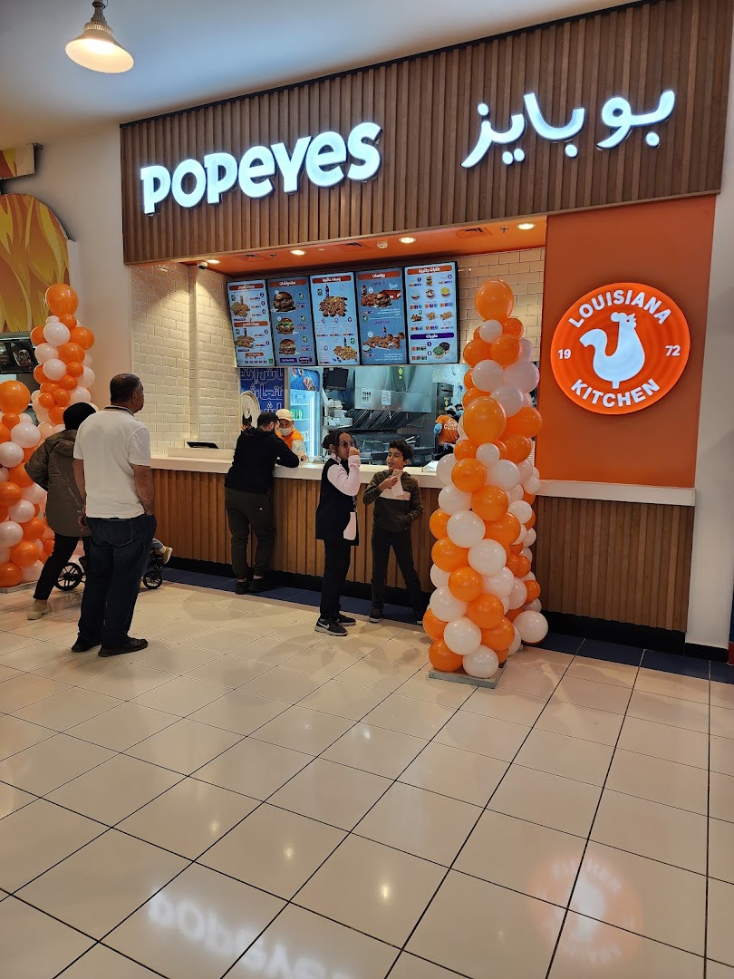 Popeyes restaurant with a bright orange and white decor, featuring a menu board and customers.