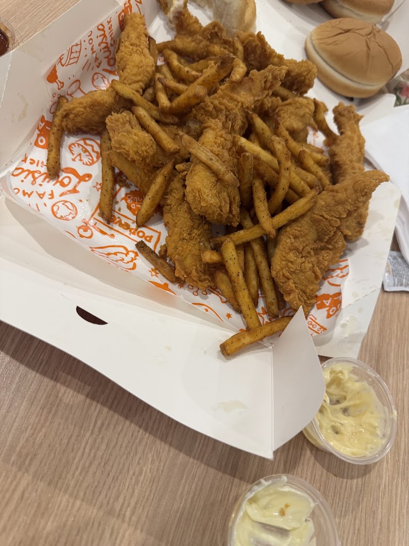 A box of Popeyes chicken tenders and fries with dipping sauce on a wooden table.