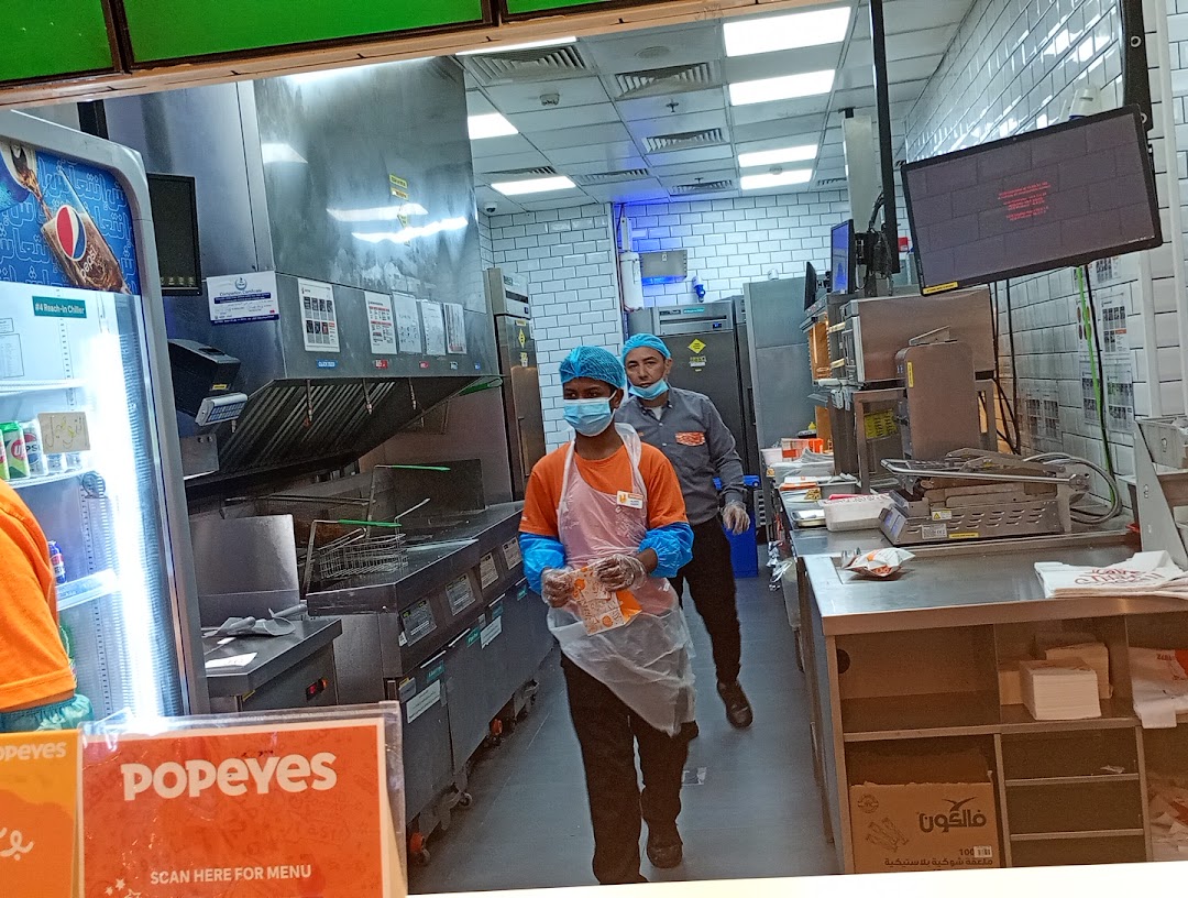 Popeyes kitchen with staff preparing food and a display of drinks.
