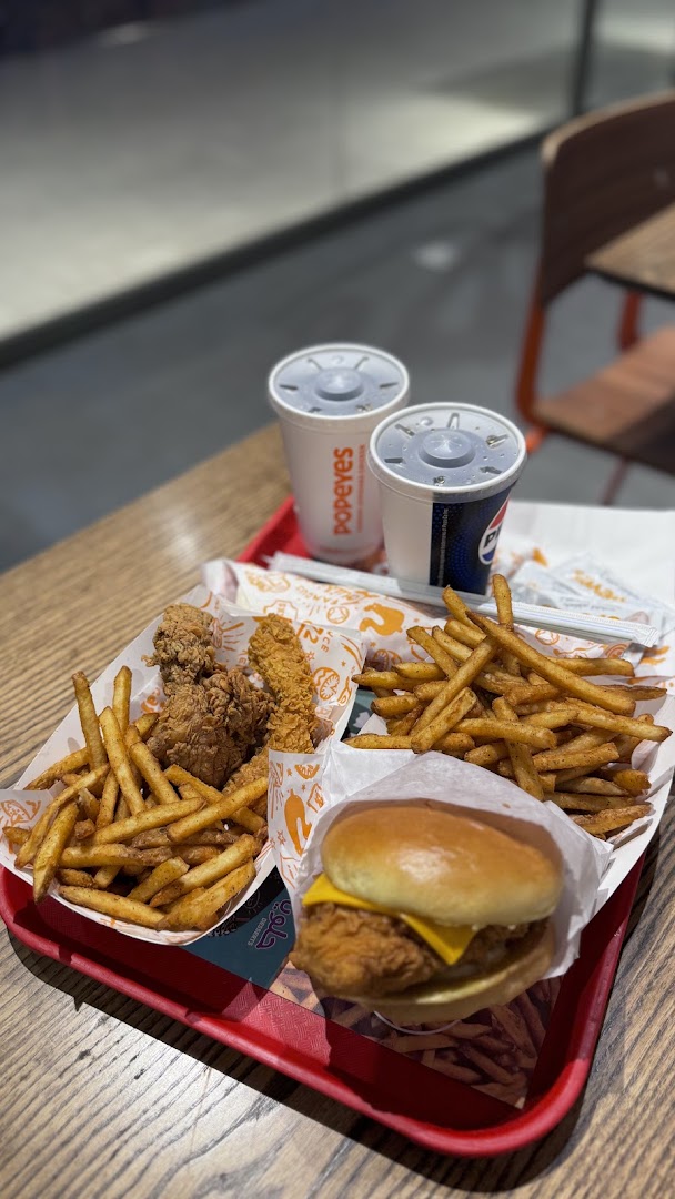 A tray of Popeyes chicken tenders, fries, a chicken sandwich, and two drinks.