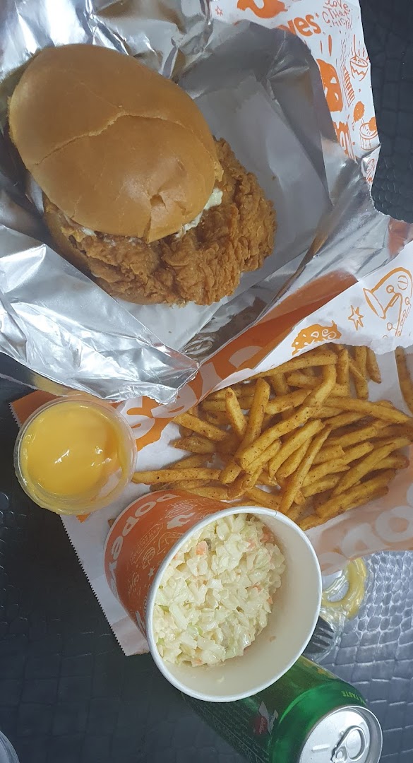 A Popeyes meal featuring a chicken sandwich, fries, coleslaw, and a dipping sauce.