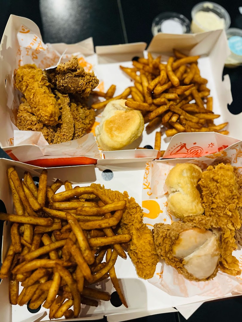 A close-up view of Popeyes fried chicken, fries, and biscuits in takeout boxes.