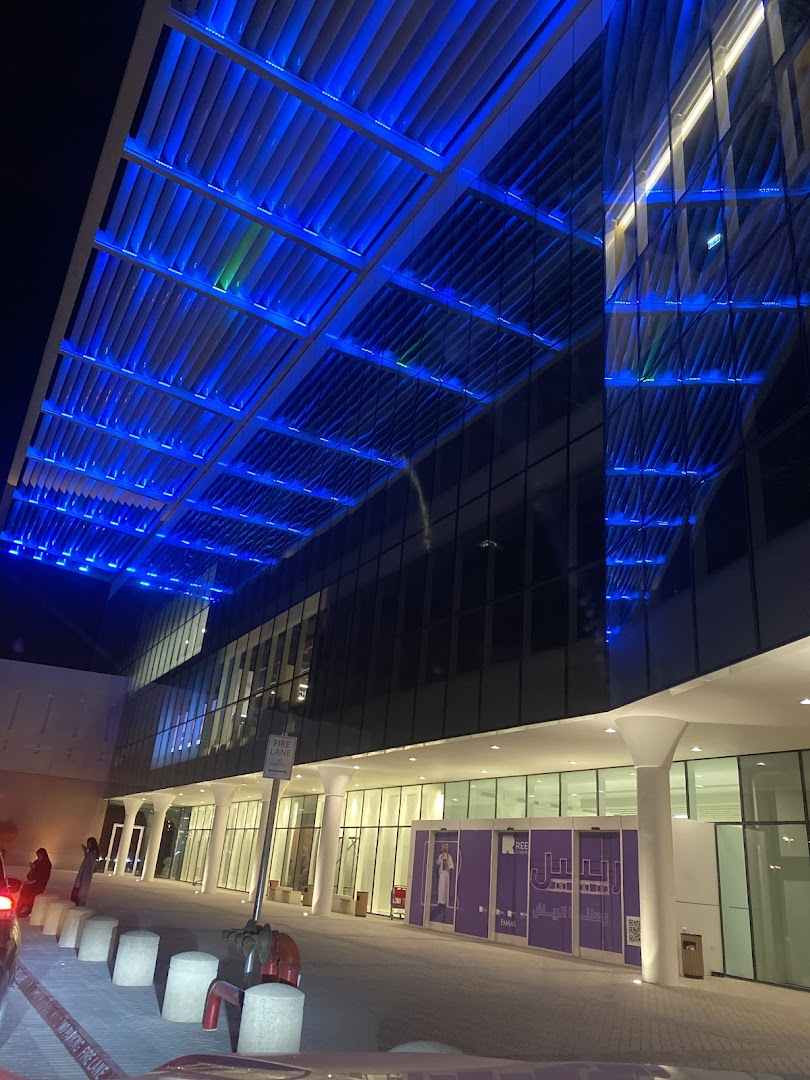 Modern building entrance at night with blue illuminated ceiling and glass facade.