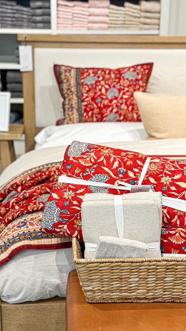 A beautifully made bed with a red floral quilt, accent pillows, and a basket of folded linens.