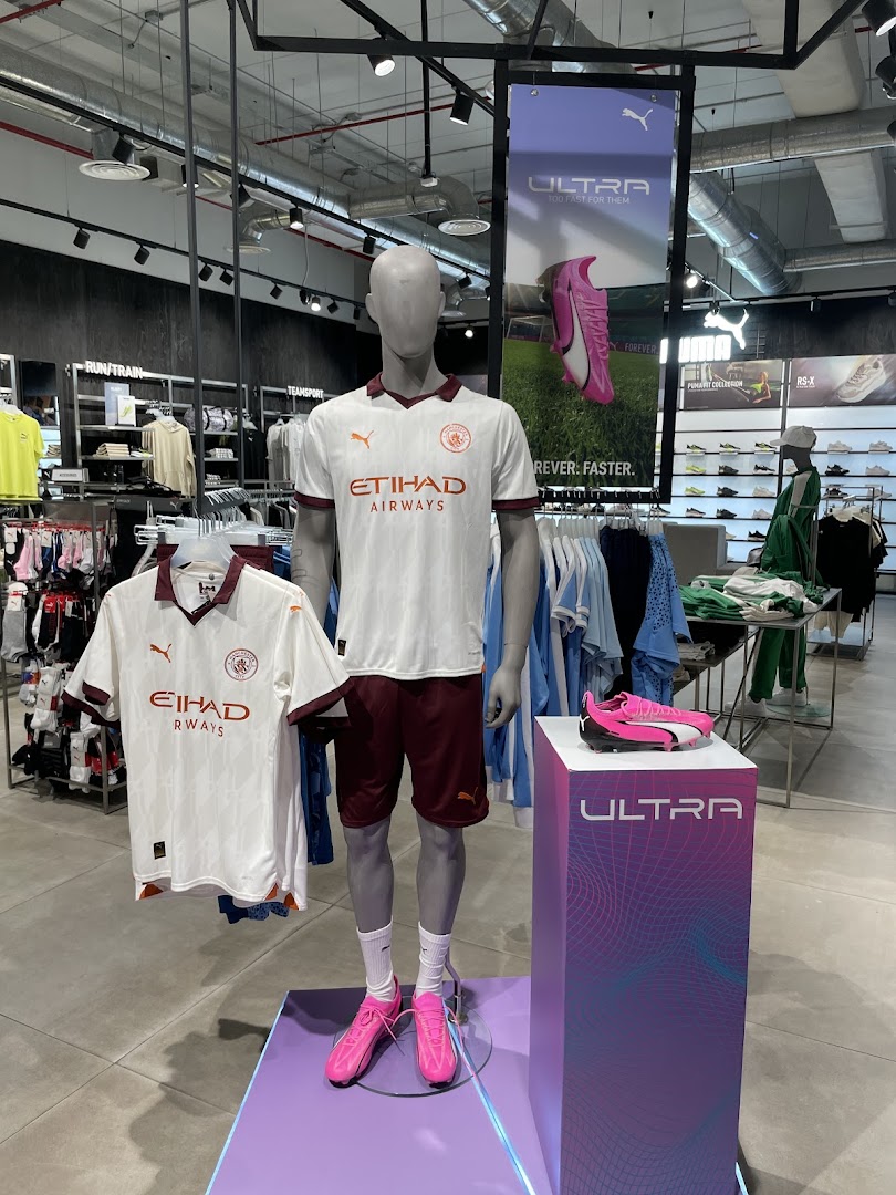 Mannequins display Puma football kits and shoes in a brightly lit retail store.
