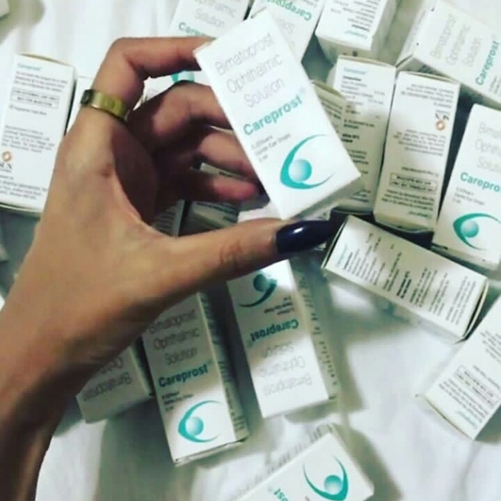 A hand holds a box of Careprost eyelash growth serum surrounded by many other boxes.