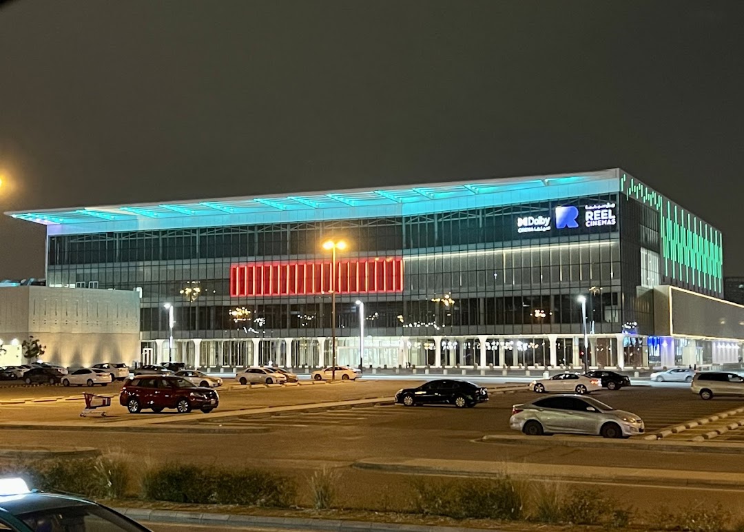 A modern cinema building with illuminated signage and a parking lot at night.