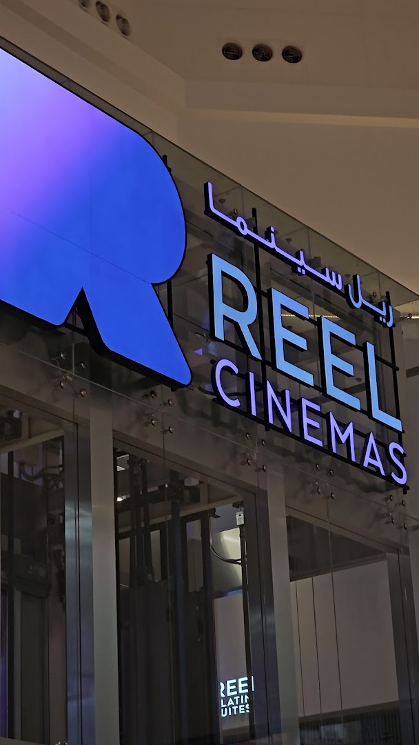 The illuminated Reel Cinemas logo and Arabic text on a glass storefront.