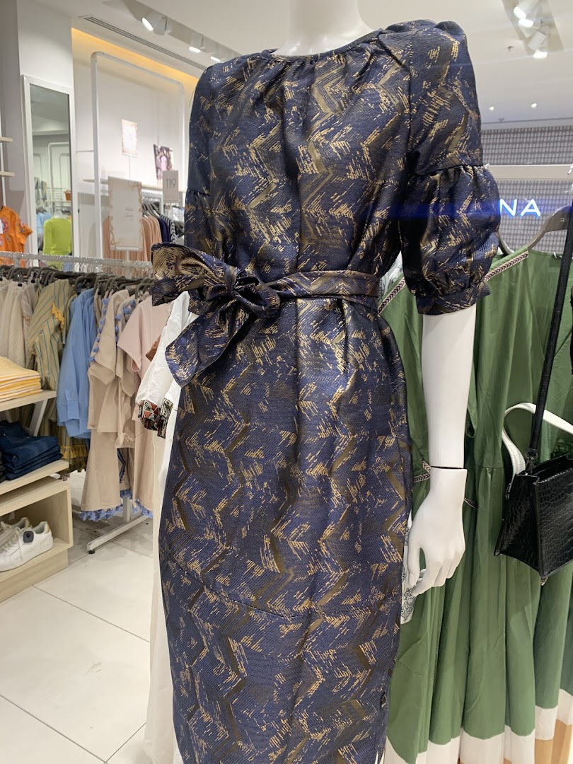 A mannequin displays a navy blue dress with a gold abstract pattern and a matching belt.