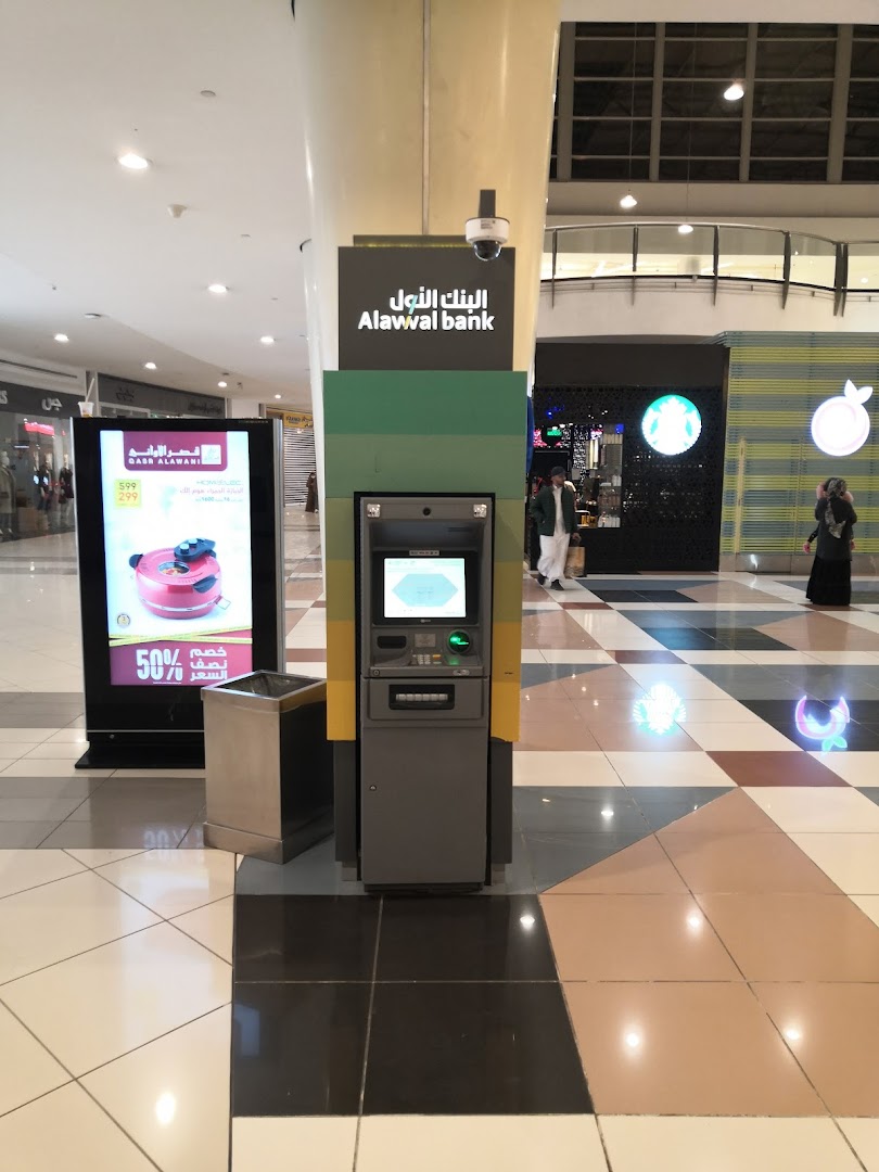 An Alawal Bank ATM is located in a shopping mall with a digital advertisement nearby.