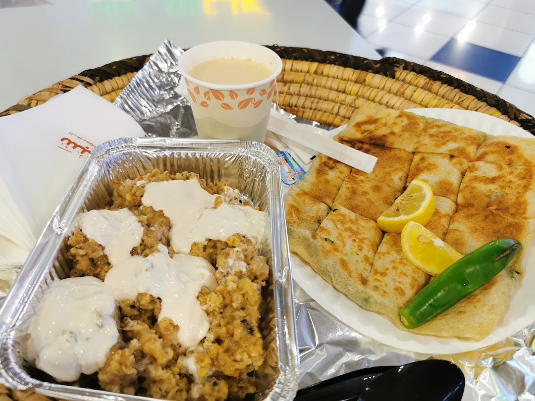 A close-up of a meal from Saba Restaurant, featuring a foil container of food with sauce and a plate of flatbread with lemon and pepper.