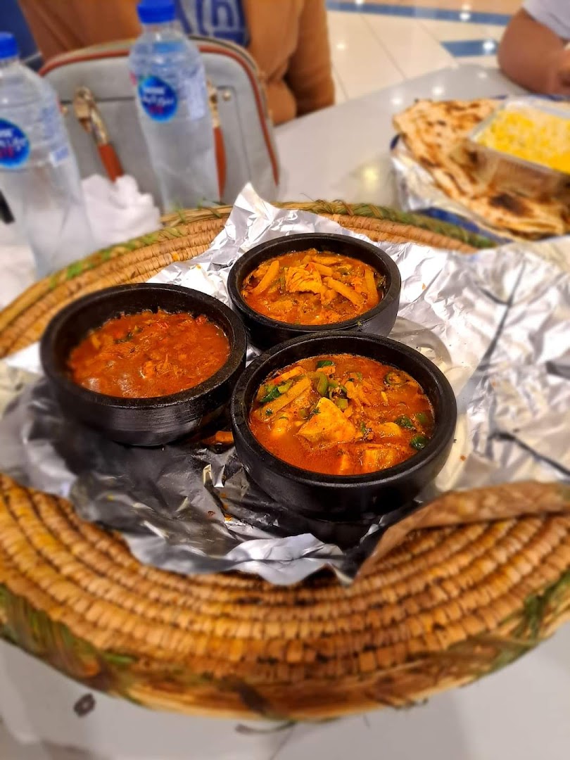 Three bowls of savory stews served in a woven basket with flatbread and rice.