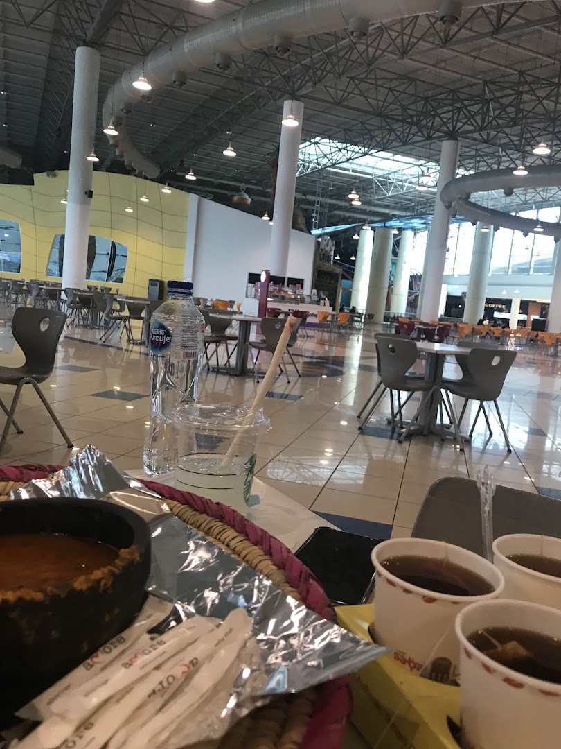 A close-up of food and drinks on a table in a spacious, modern food court.