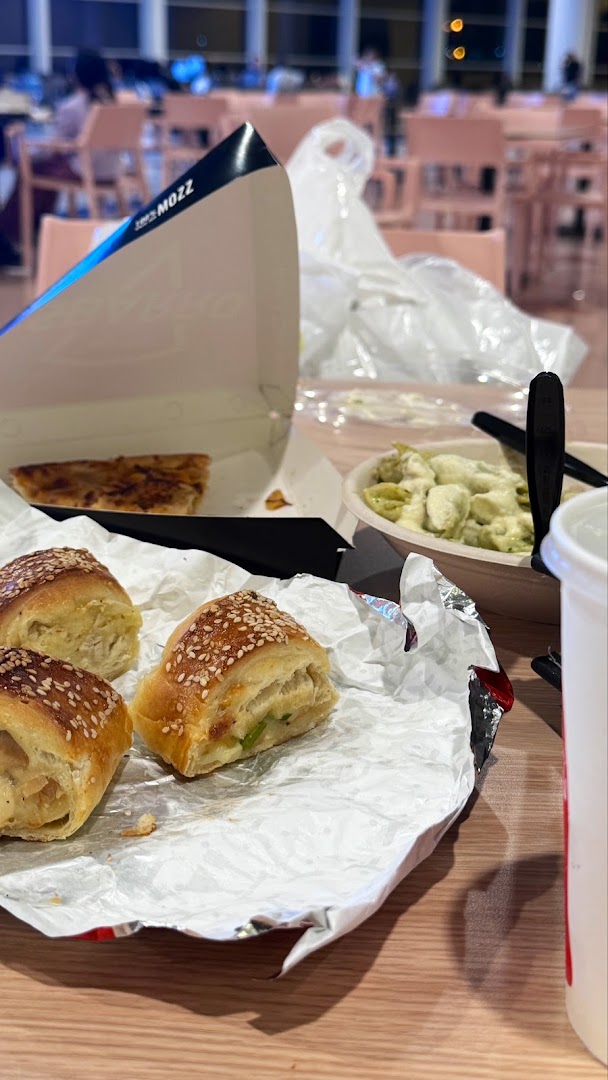 A table with Sbarro food items including rolls, pizza, pasta, and a drink.