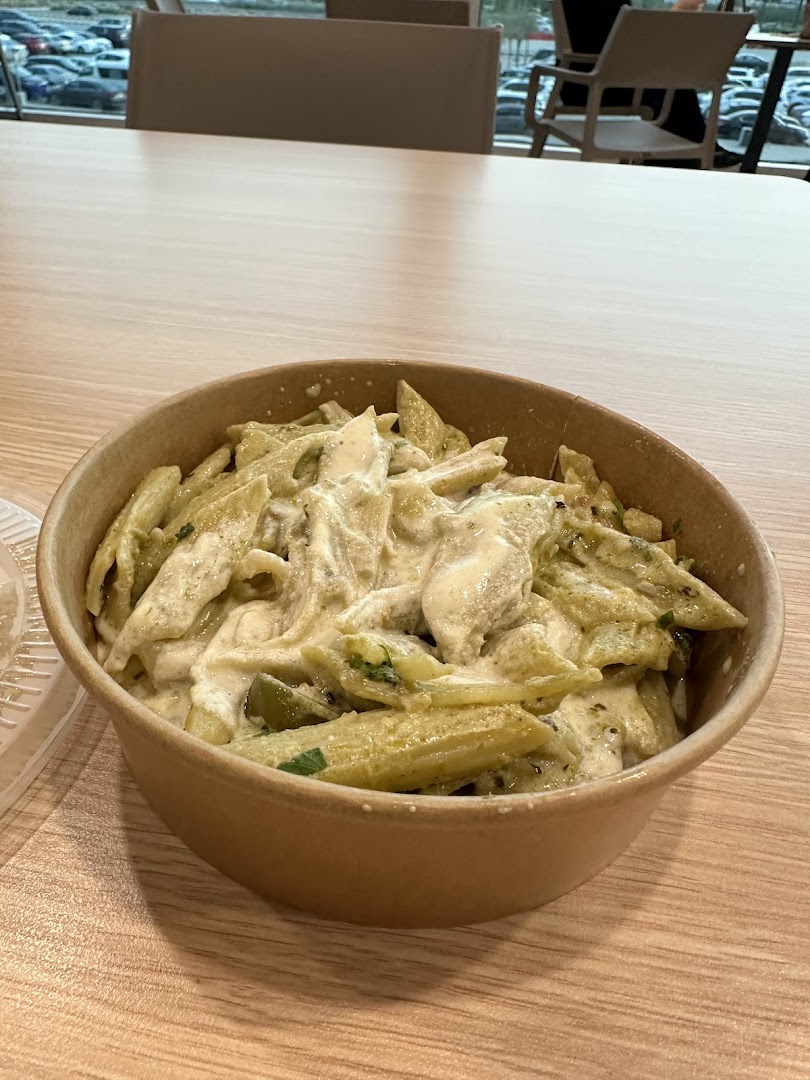 A bowl of creamy pesto pasta with chicken served on a wooden table.