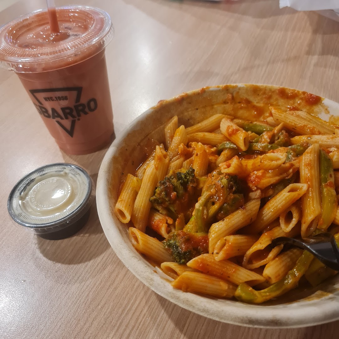 A bowl of penne pasta with broccoli and sauce, next to a drink and a side of dip.