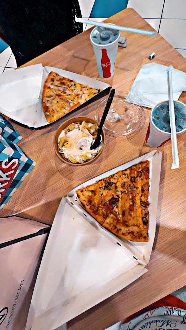 Sbarro pizza slices, drinks, and a side dish on a wooden table.