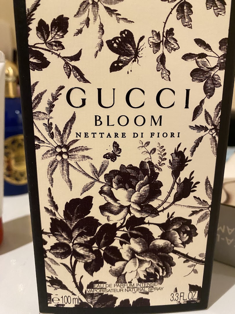 A close-up of a Gucci Bloom Nectar di Fiori perfume bottle with floral and butterfly designs.
