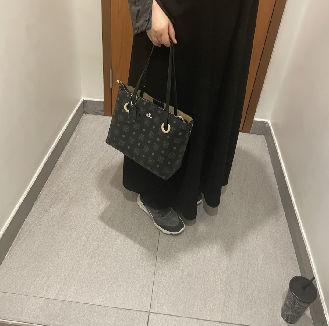 A person holding a stylish patterned handbag and wearing sneakers.