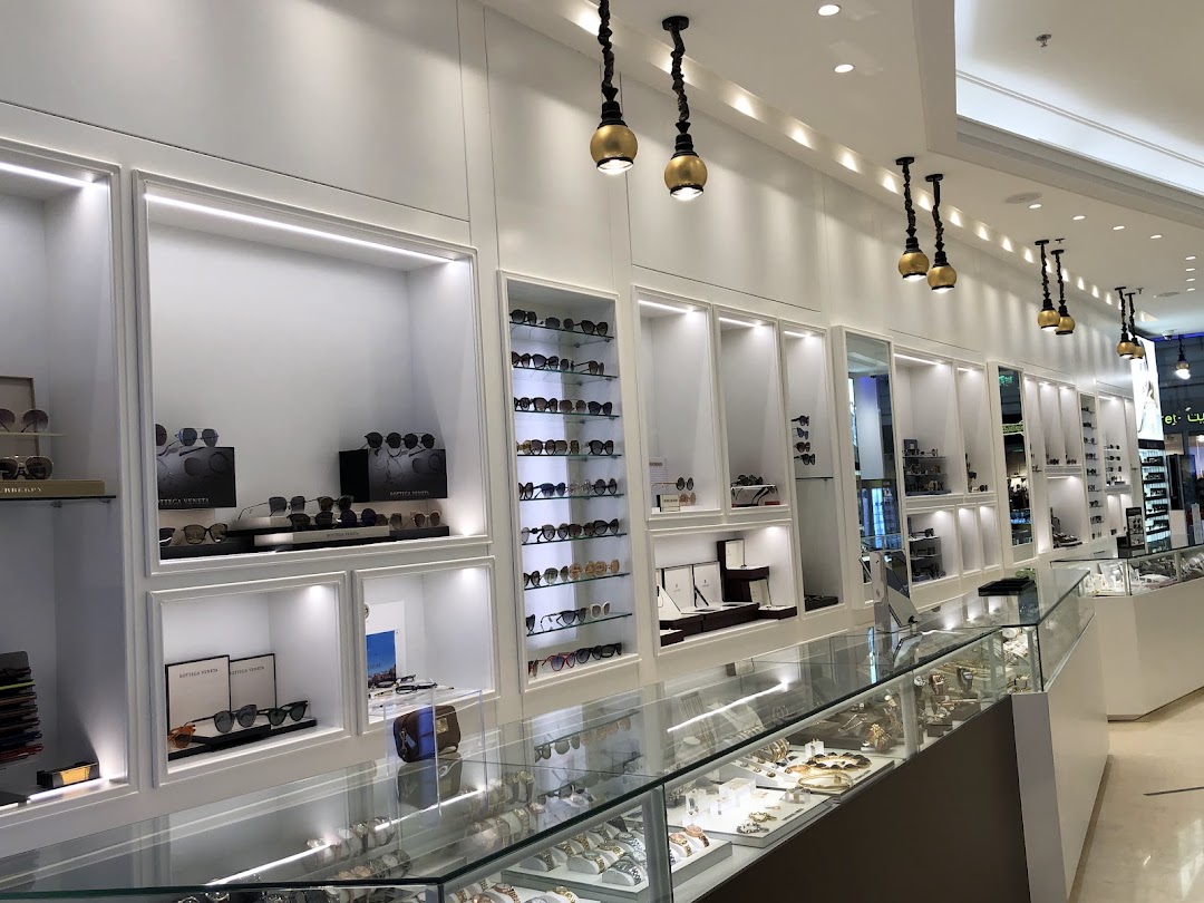 Interior view of Shaden Stores, showcasing a wide selection of sunglasses and watches displayed in illuminated shelves and glass cases.