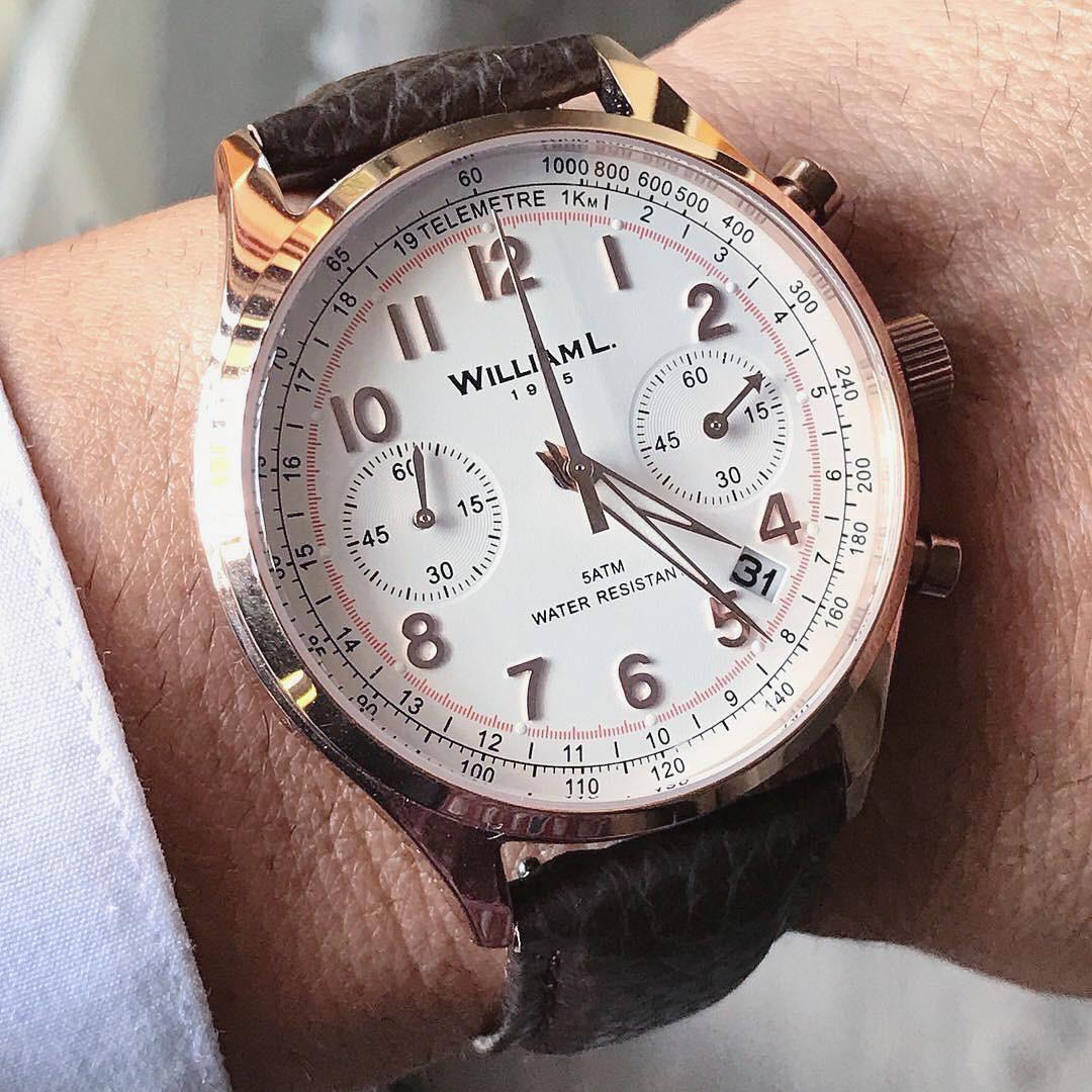 A close-up shot of a man wearing a gold-toned wristwatch with a white dial and a dark leather strap.
