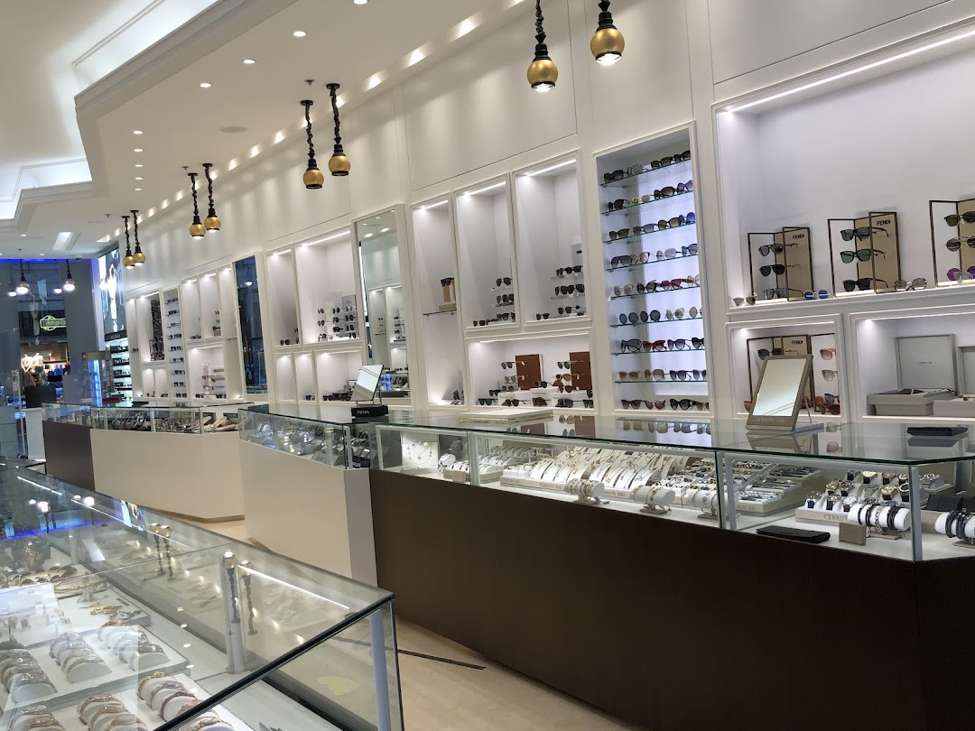 Interior view of a modern retail store displaying sunglasses and watches in illuminated display cases.