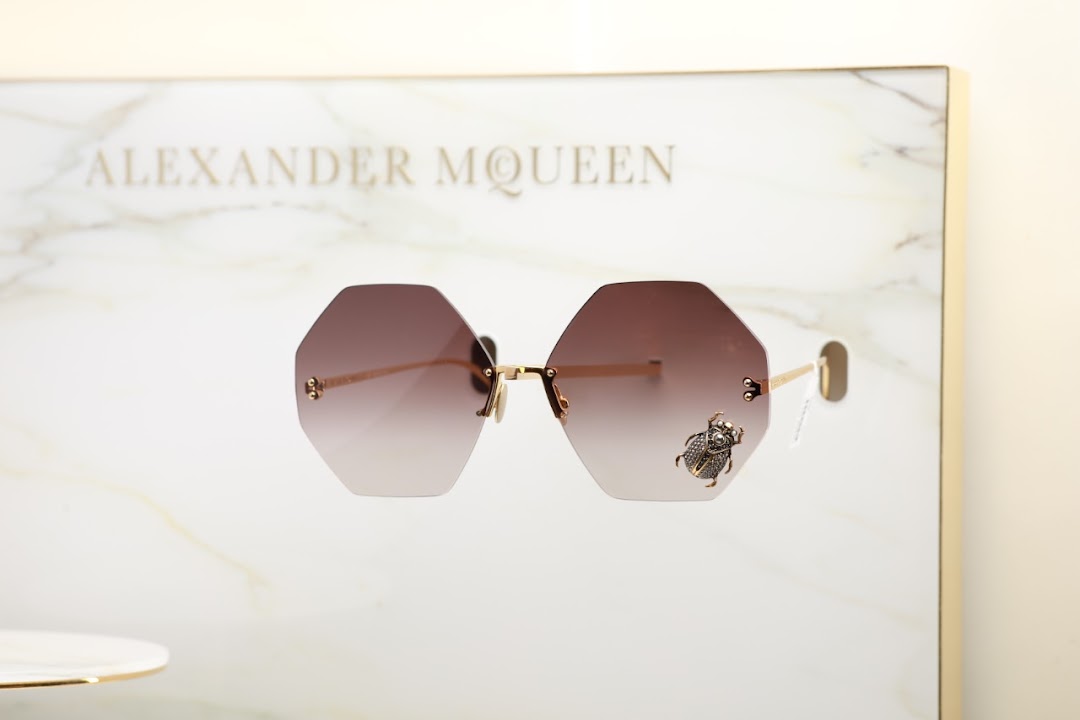 Alexander McQueen sunglasses with a bee embellishment displayed on a marble-like surface.