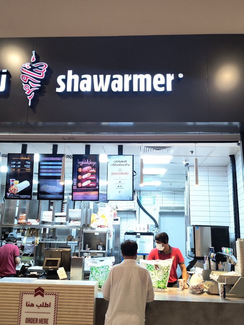 A Shawarmer shop with staff serving customers and menus displayed.