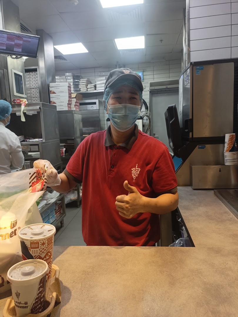 A Shawarmer employee in uniform gives a thumbs up while preparing an order.