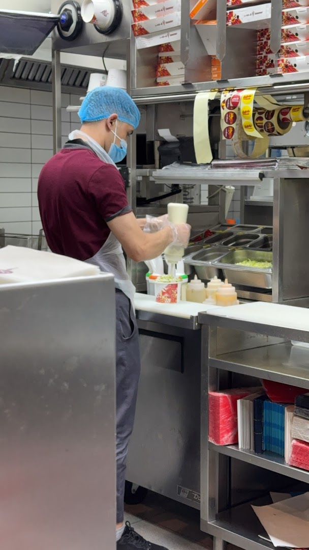 A chef prepares food in a clean kitchen, adding sauce to a dish.