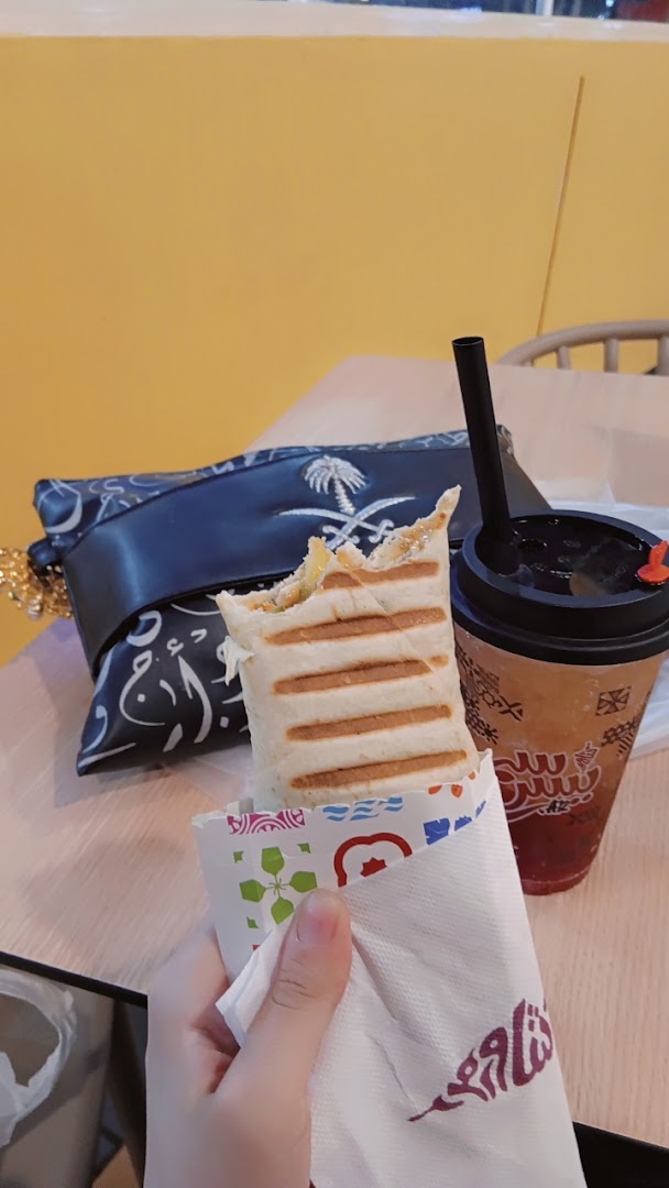 A person holds a grilled shawarma wrap and a drink from Shawarmer.