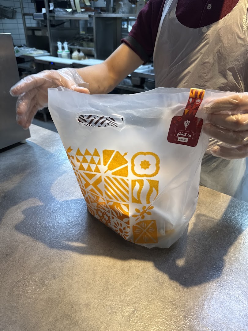 A person in gloves holds a branded takeaway bag from Shawarmer.