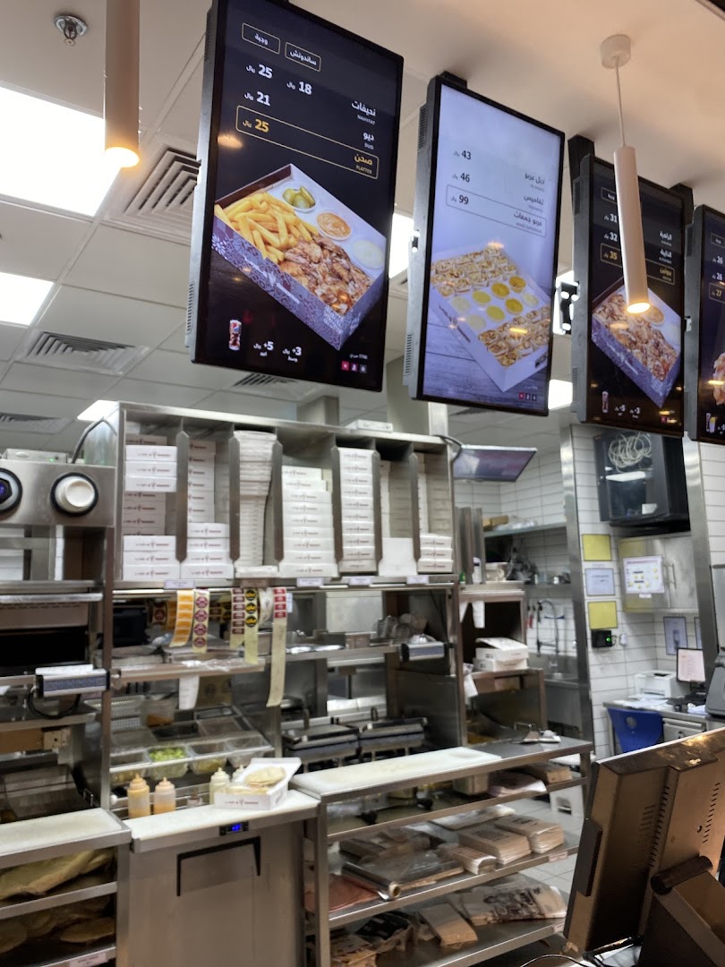 Digital menu boards displaying shawarma platters and other food items at Shawarmer.